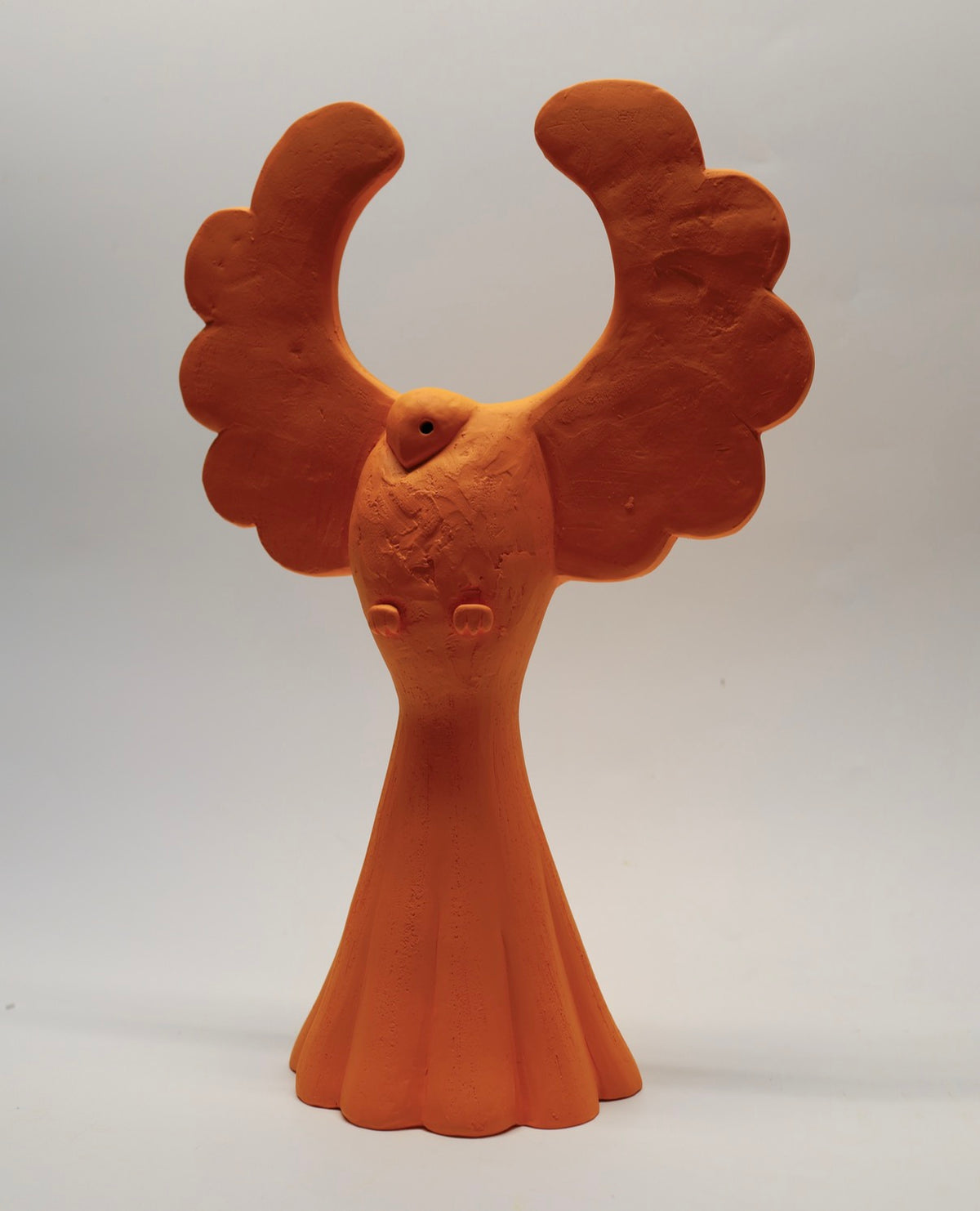 Champion is a stunning ceramic orange bird with wings lifted and his head cocked at an angle in flight beneath a forest canopy.