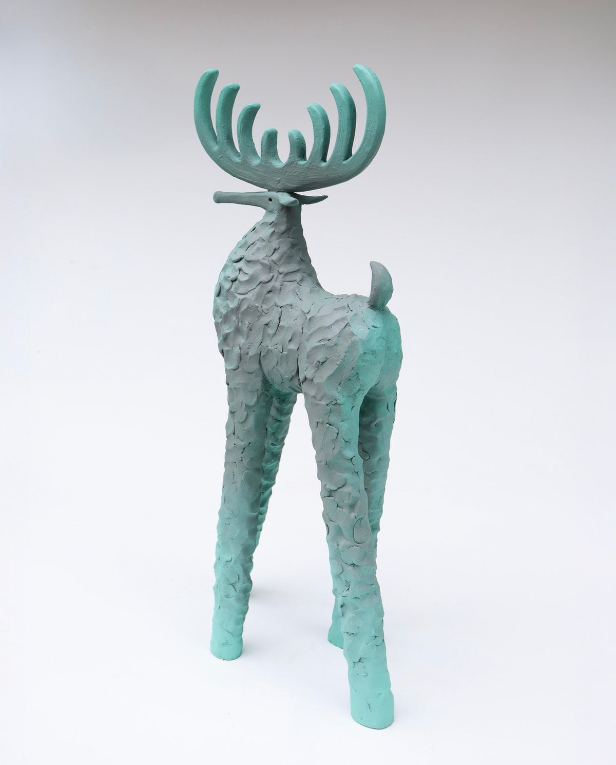 A stylized deer ceramic sculpture with textured, body legs and antlers, painted in a teal-green color