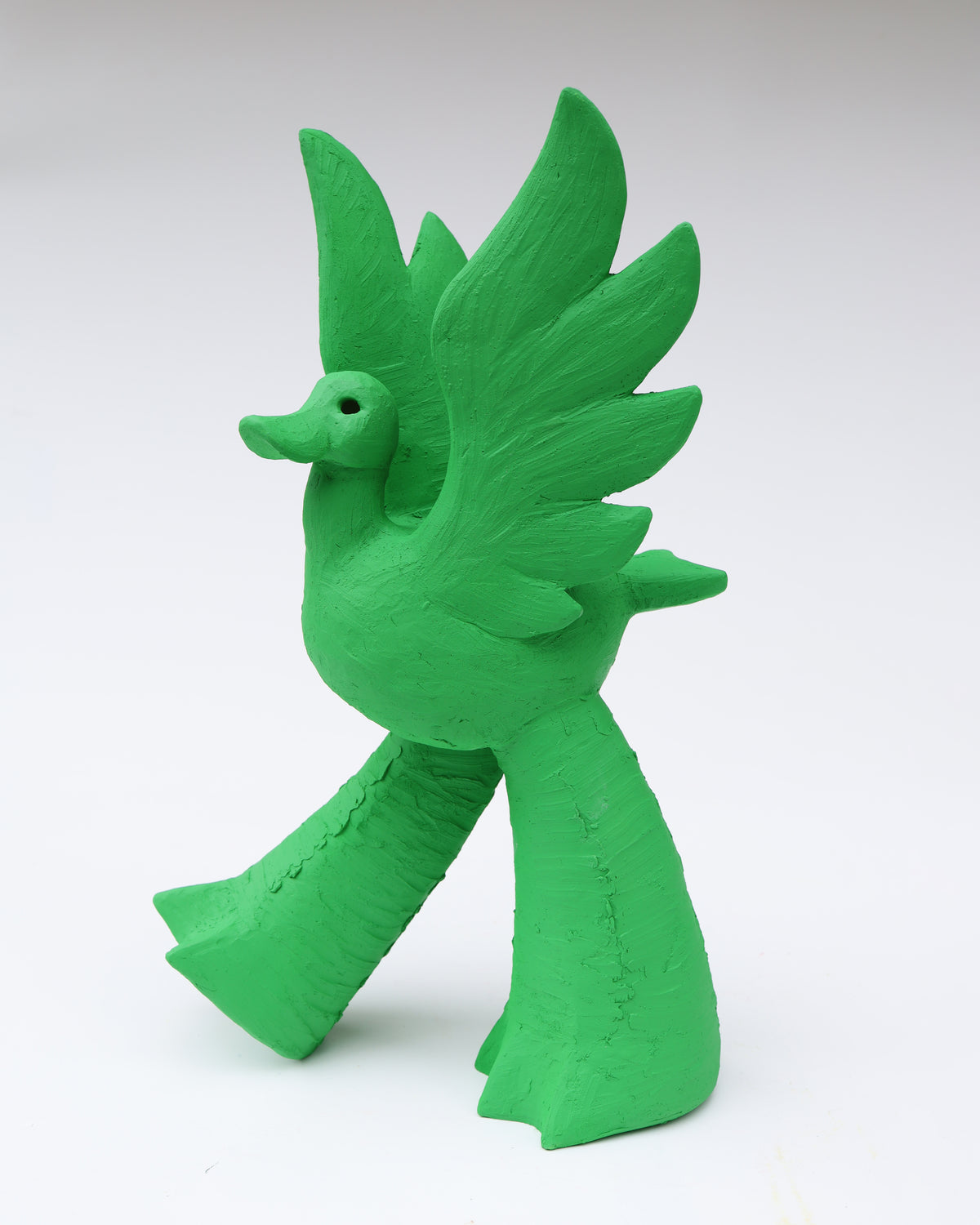 A bright green, stylized duck ceramic figure with textured wings and legs in the style of pop folk art