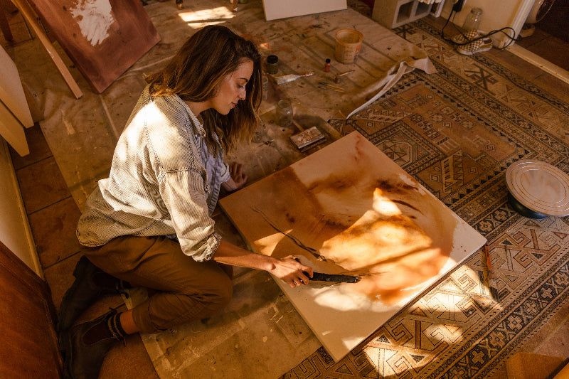 Artist Danielle Hutchens working on a large painting using charcoal and natural pigments on the floor in her studio