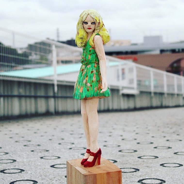 A view of Monet outside. She is a wood carved female figure in a green flower dress  with red velvet high heels, by Hideki Iinuma, Japanese artist.