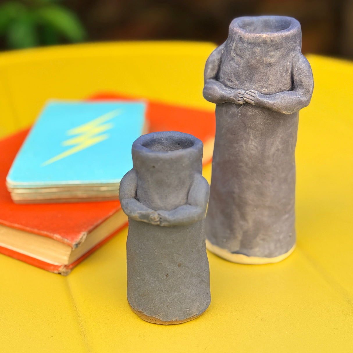 Two black grape clay hug candle holders on a yellow surface with a deck of cards and book in the background