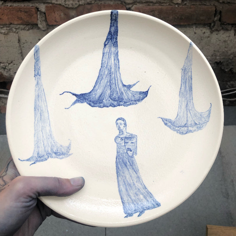 Ceramic plate with blue watercolor painting of trumpet flowers and a drama statue.