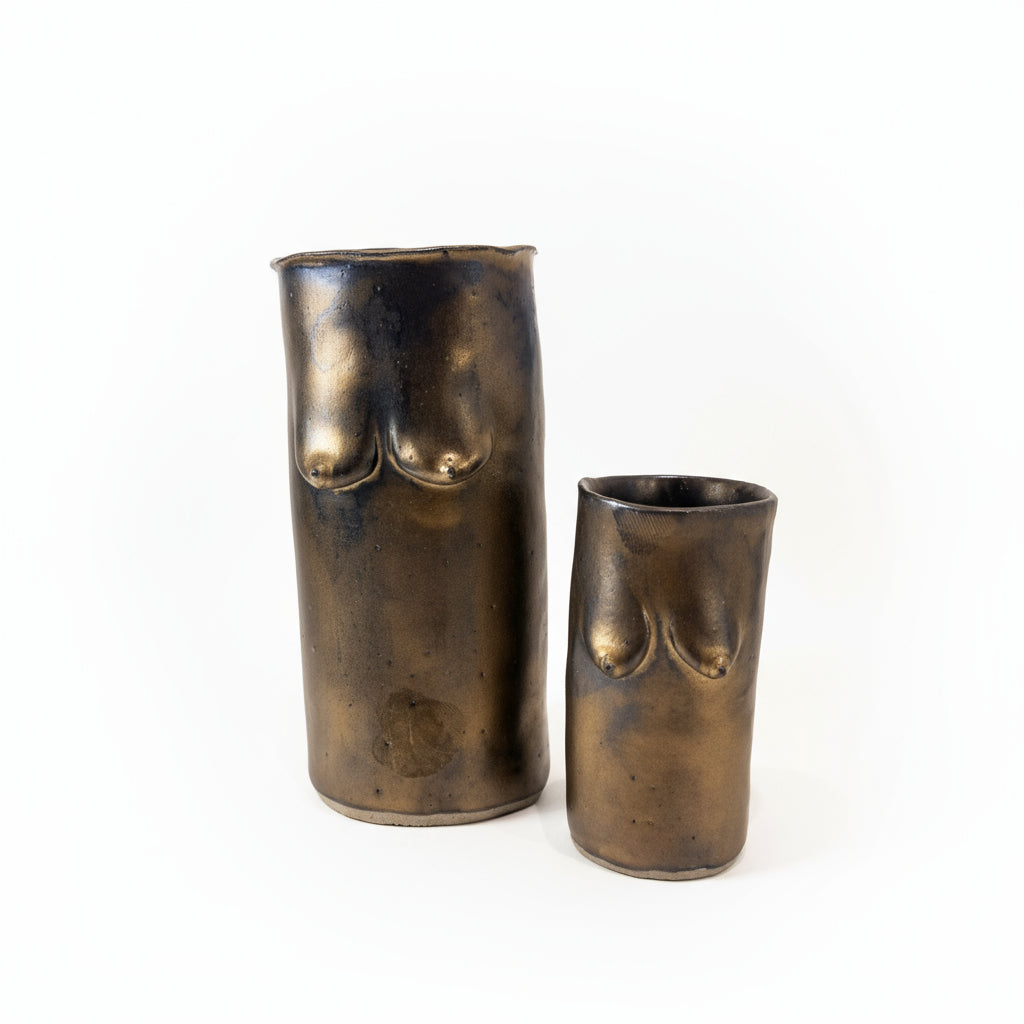 Two bronze-colored cylindrical vases and cup with sculpted breasts in ceramic on a white surface.