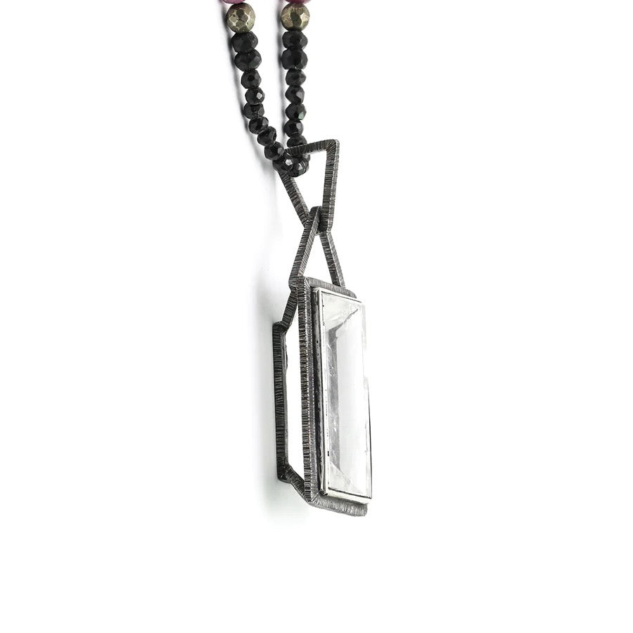 This simple yet elegant pendant is comprised of a framework of etched and oxidized silver, which encases a singular rough-hewn rock crystal.