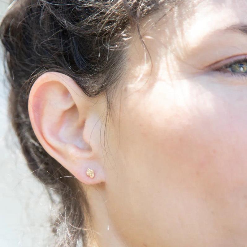 Idun mini flower stud posts on model. These petite flower earrings are cast in 14K yellow gold.