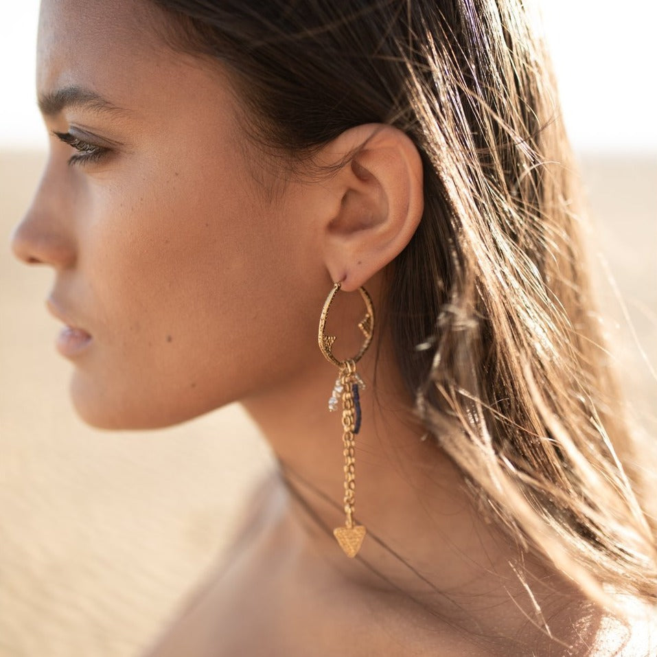 A flying arrow merging with a future magic. Arrows of possibility, formed from velvet light, ride the restless winds of our longing. The Regal Arcus dangling hoop is embellished with arrows, deep ocean pearls for depth, and mountain lapis for height.