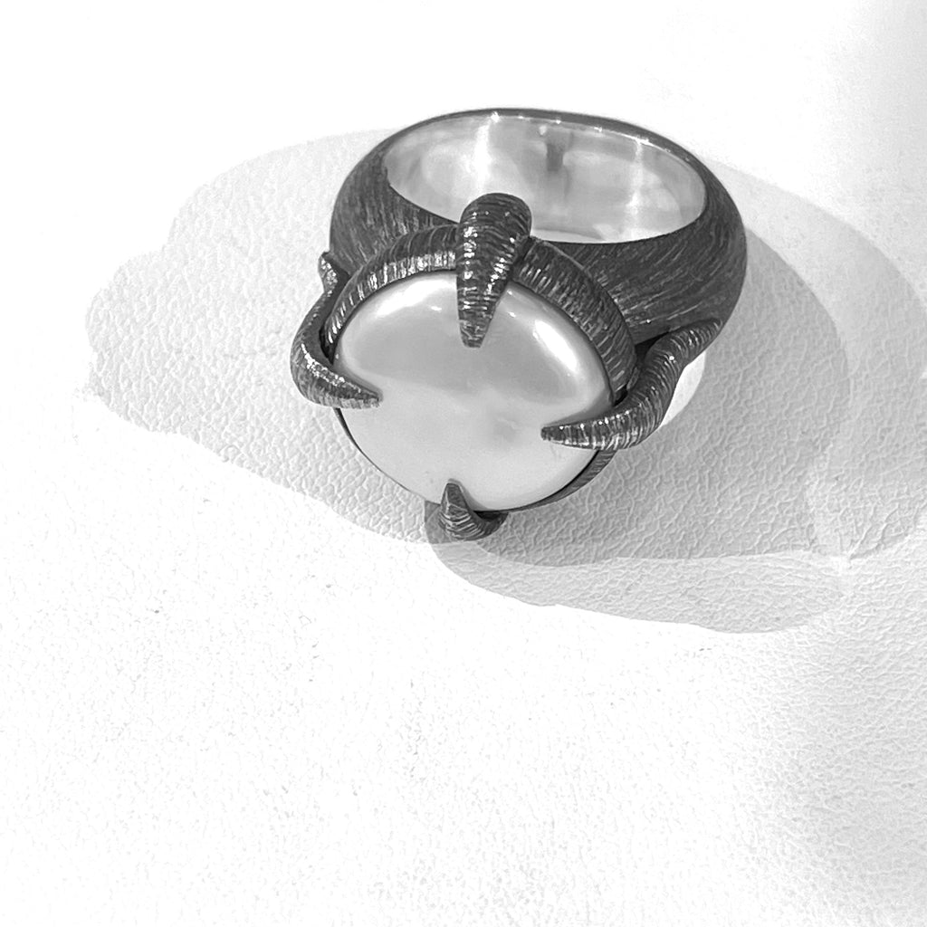 An edgy and modern pearl ring with a baroque pearl clasped within etched and oxidized silver prongs. A contrast of textures by Mariella Pilato.