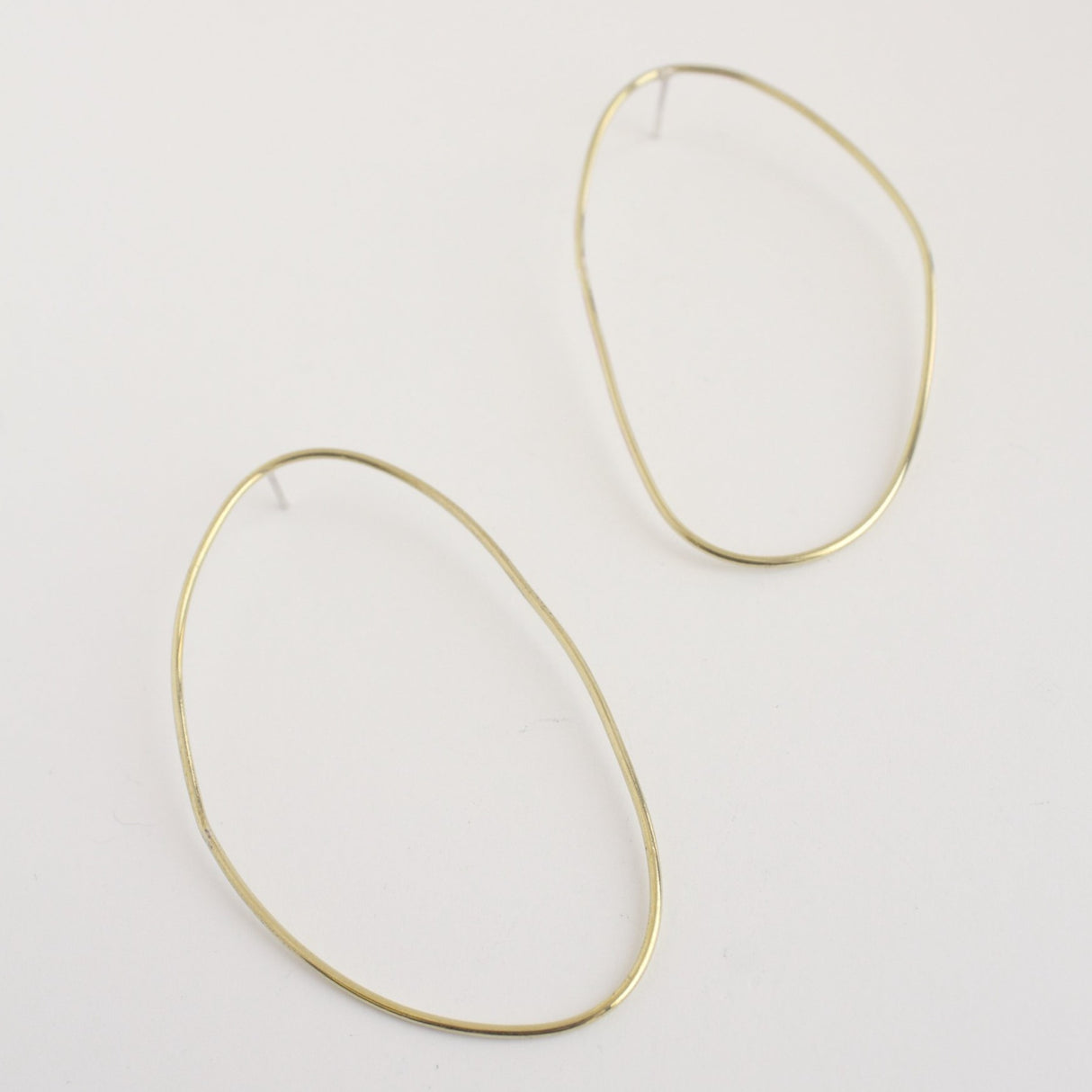 Asymmetrical oval olive-shaped brass earring hoops boast a sophisticated yet modern aesthetic.