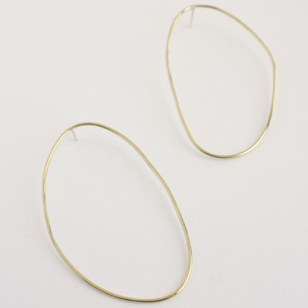 Asymmetrical oval olive-shaped brass earring hoops boast a sophisticated yet modern aesthetic.