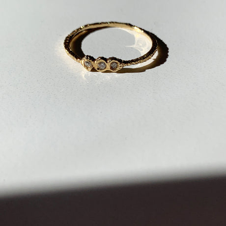 Danielle Welmond adds texture to your ring stack with this elegant yellow gold super skinny etched band set with three white diamonds.