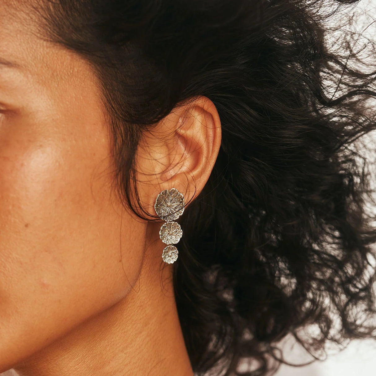 Close-up of a woman wearing a silver triple drop lily papd earring