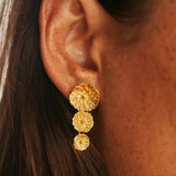 Close-up of a woman wearing gold lily pad drop earrings