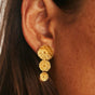 Close-up of a woman wearing gold lily pad drop earrings