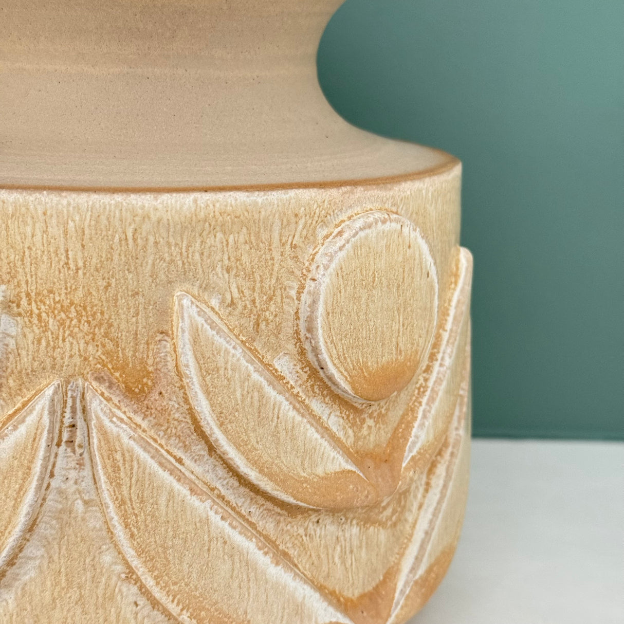 Wheel thrown vase with hand carved relief flower designs. In natural glaze. Detail.