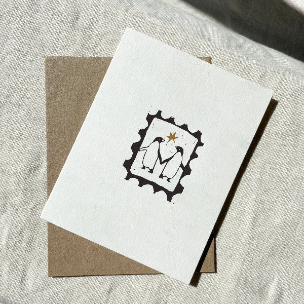 White greeting card with black frame and inside features two penguins and a star