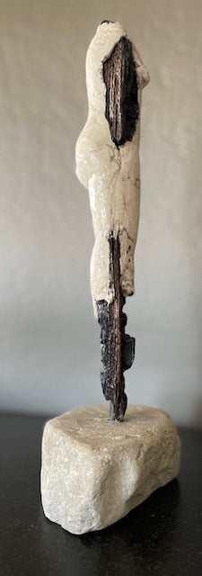 Standing female figure sculpted from clay and surrounding burnt wood, mounted on stone. Side view