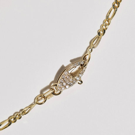 A solid 14k gold figaro chain with a custom pavé double-sided diamond clasp to feature as a design element. 