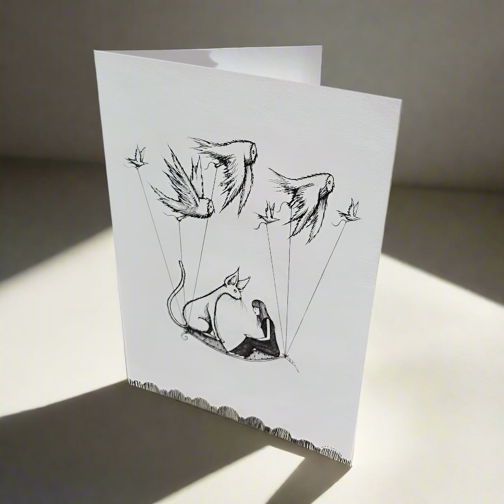 Greeting card with pencil and pen drawing of a cat and girl on a magic carpet, carried by birds through the sky