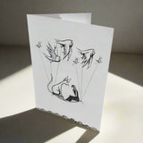 Greeting card with pencil and pen drawing of a cat and girl on a magic carpet, carried by birds through the sky