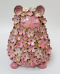 A pink ceramic figurine in a meditative sitting pose, covered in layered pink cherry blossom petals with gold-toned edges