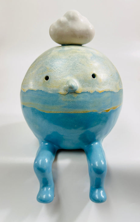 A ceramic figurine of a seated blue cloud man character with a small white cloud on its head, glazed in various shades of blues and white and with yellow accents.
