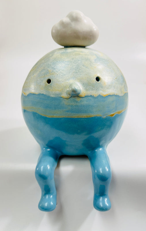 A ceramic figurine of a seated blue cloud man character with a small white cloud on its head, glazed in various shades of blues and white and with yellow accents.