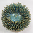 A ceramic prickly man sculpture with a glossy blue-green glaze and light tan tips on its spines.