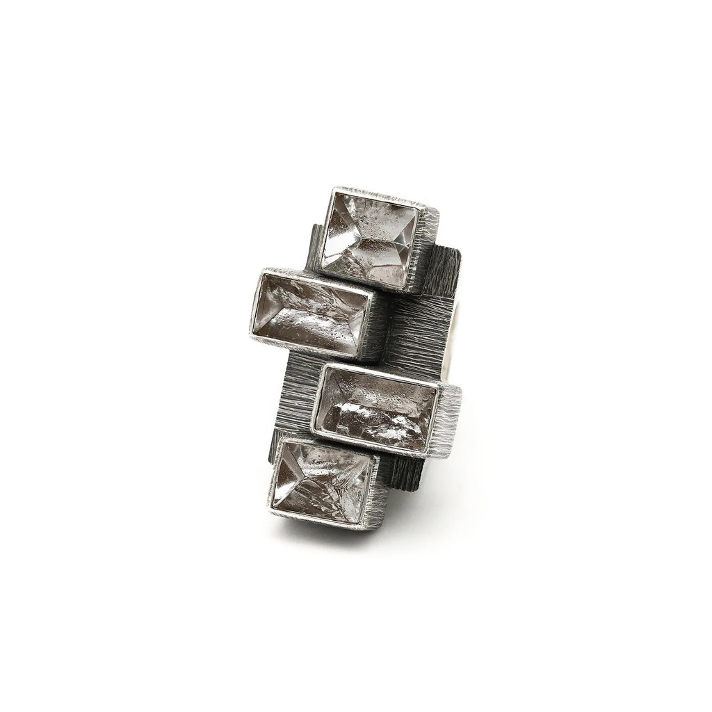 Top view of rough-hewn crystal ring. Etched and oxidized silver settings of differing heights and alternating position to one another encase four natural faced rock crystals.