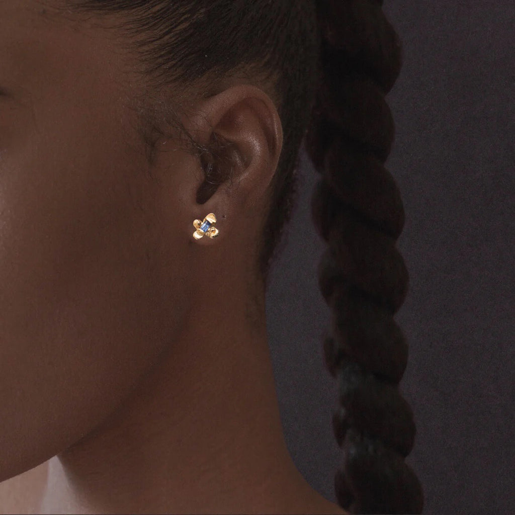 Idun is a four petal 14k yellow gold flower stud earring with ethically mined Sapphires from Montana, shown on model.