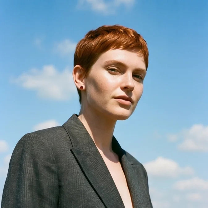 Female with short red hair wearing a grey blazer and garnet 3 prong martini stud earrings