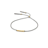 A delicate grey cord bracelet featuring a central cluster of small 14k gold filled beads and adjustable grey tassel ends, displayed on a clean white background.