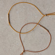 Close-up of thin braided silk cord friendship bracelets with small 14k gold filled bead accents and tassels