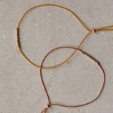 Close-up of thin braided silk cord friendship bracelets with small 14k gold filled bead accents and tassels