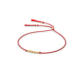 A delicate red silk cord bracelet featuring a central cluster of small 14k gold filled beads and adjustable red silk tassel ends, displayed on a clean white background.