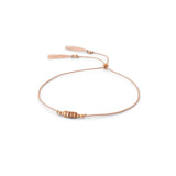 A delicate blush silk cord bracelet featuring a central cluster of small rose gold beads and adjustable blush tassel ends, displayed on a clean white background.
