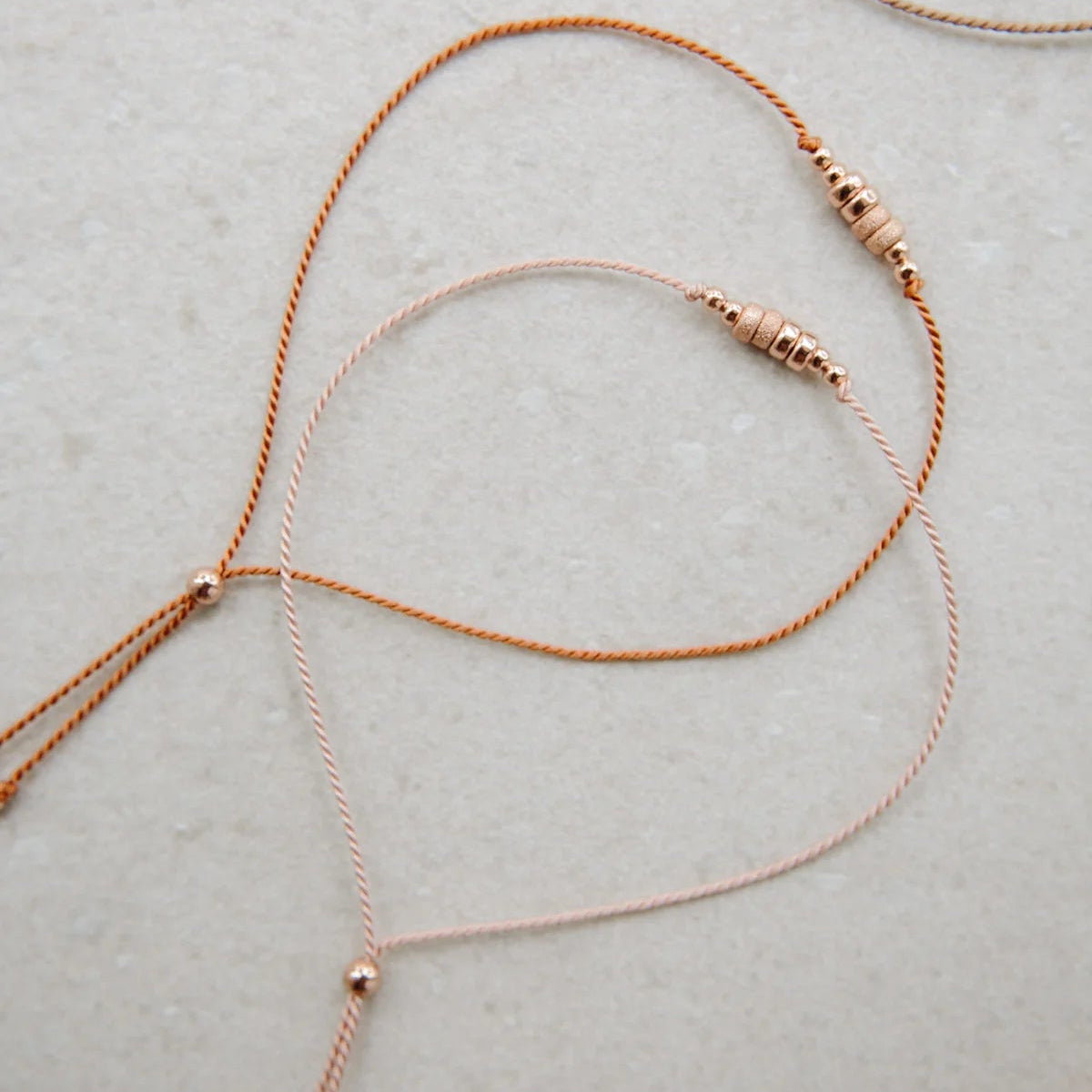 Close-up of thin braided silk cord friendship bracelets with small 14k rose gold bead accents and tassels
