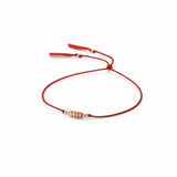 A delicate red silk cord bracelet featuring a central cluster of small rose gold beads and adjustable red tassel ends, displayed on a clean white background.