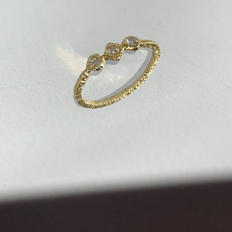 Danielle Welmond yellow gold super skinny smooth band set with three white diamonds in textured bezel settings. One diamond shaped diamond sits between two round diamonds.