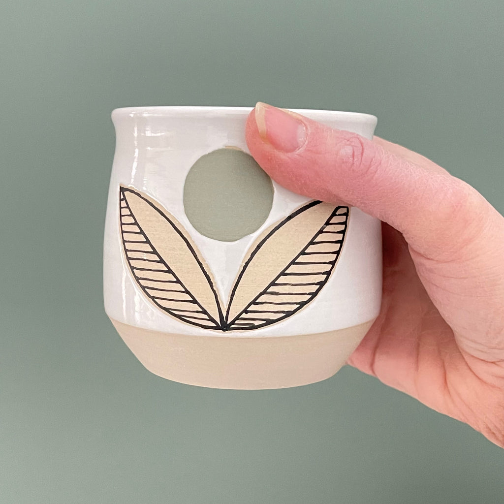 Get cozy with a warm cup, wheel thrown and decorated with a Scandinavian aesthetic. This substantial beauty of a cup, tumbler or handle-less mug comes in 14oz to hold your favorite beverage or soup. We love the pop of color with a flower pattern in a green palette.