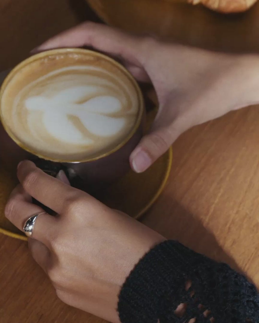Carina Hardy Pearl Dome Ring on Model sitting at a coffee shop drinking coffee and eating a croissant