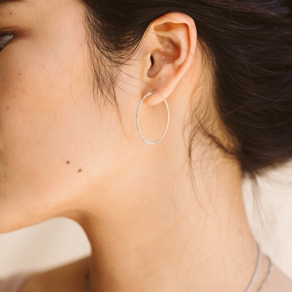 Abacus Row Pan hoops feature unexpected patterning of gold among matte glass beads. One earring within each pair features a gold-beaded segment along the backside of the hoop. Shown on model.