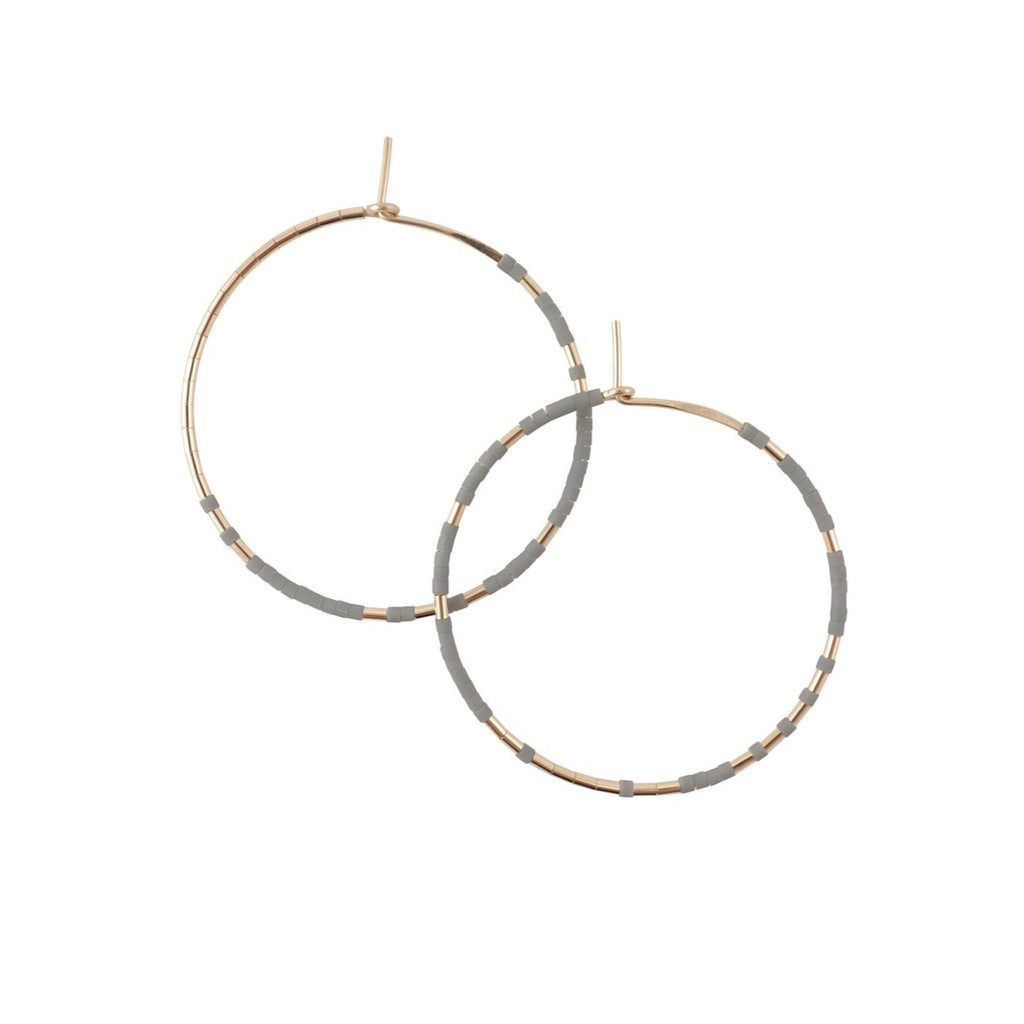 With Abacus Row's Pan Hoops, designer Christine Trac showcases an asymmetrical design of unexpected patterning of gold among matte glass beads. A cement grey tone.