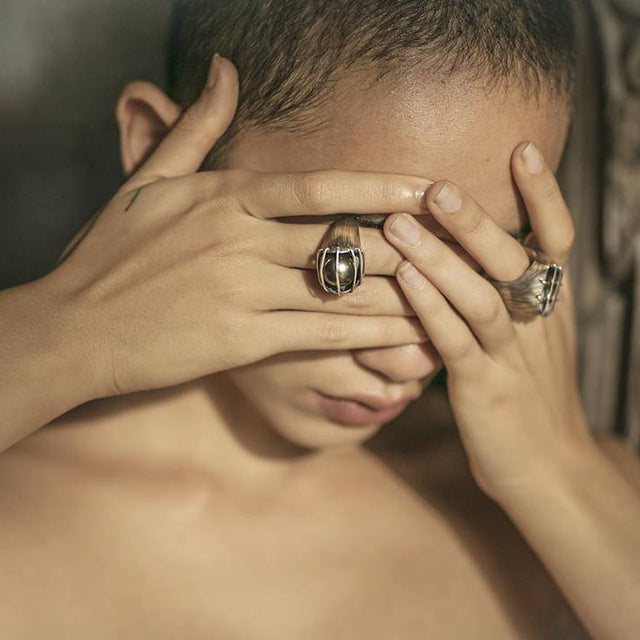 A luminous, natural inky-black colored Tahitian black pearl is enclosed in a heavily etched container, held in place by parallel bands of high polished silver designed by Mariella Pilato. Shown on model.