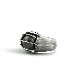 A luminous, natural inky-black colored Tahitian black pearl is enclosed in a heavily etched container, held in place by parallel bands of high polished silver designed by Mariella Pilato.