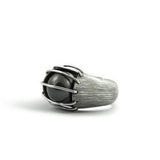 A luminous, natural inky-black colored Tahitian black pearl is enclosed in a heavily etched container, held in place by parallel bands of high polished silver designed by Mariella Pilato.